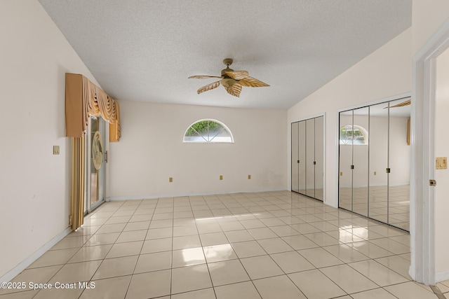 unfurnished bedroom featuring lofted ceiling, light tile patterned floors, a textured ceiling, and two closets