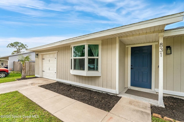 view of exterior entry featuring a garage, concrete driveway, and fence