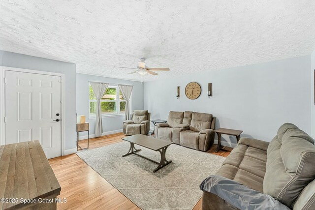 living area with light wood-type flooring, ceiling fan, baseboards, and a textured ceiling