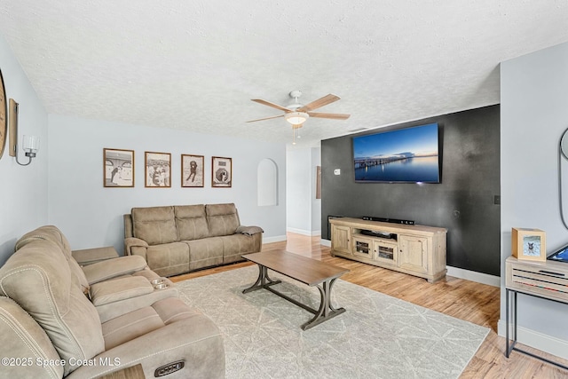 living area featuring a textured ceiling, light wood-type flooring, a ceiling fan, and baseboards