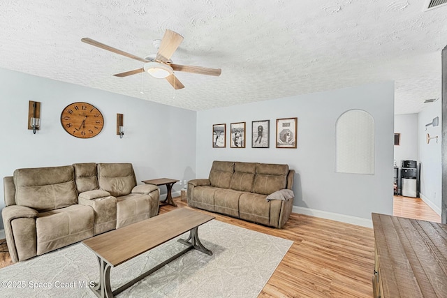 living room featuring a ceiling fan, baseboards, a textured ceiling, and light wood finished floors