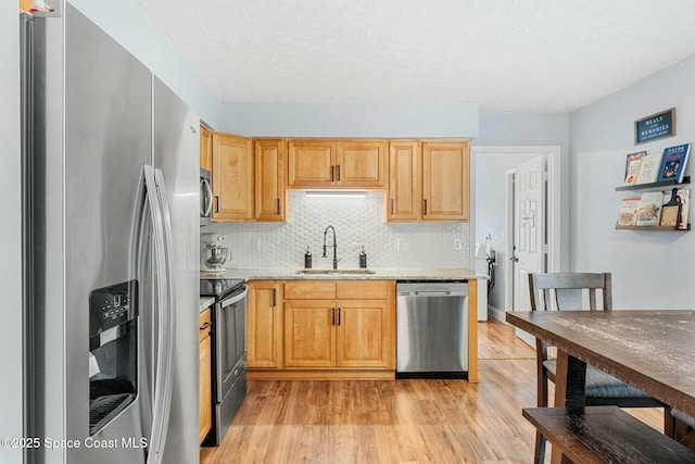 kitchen with stainless steel appliances, a sink, light wood-style floors, backsplash, and light brown cabinetry