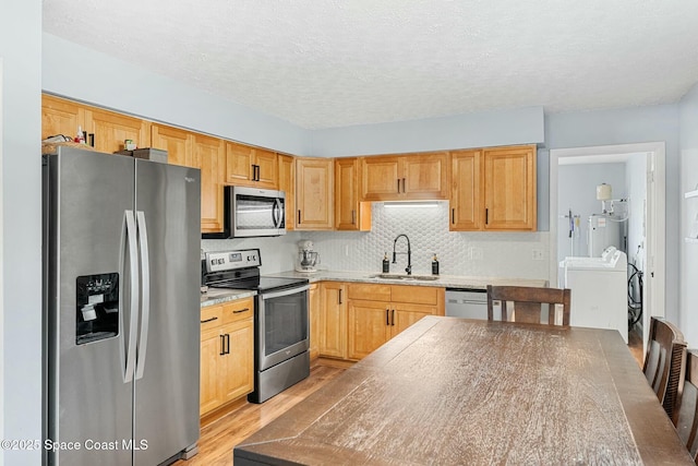 kitchen featuring tasteful backsplash, light wood-style flooring, appliances with stainless steel finishes, washing machine and dryer, and a sink