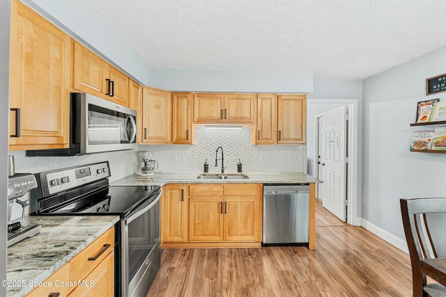 kitchen featuring light stone counters, light wood finished floors, stainless steel appliances, a sink, and baseboards