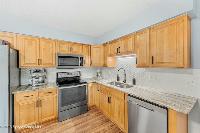 kitchen featuring light wood finished floors, tasteful backsplash, appliances with stainless steel finishes, light stone counters, and a sink