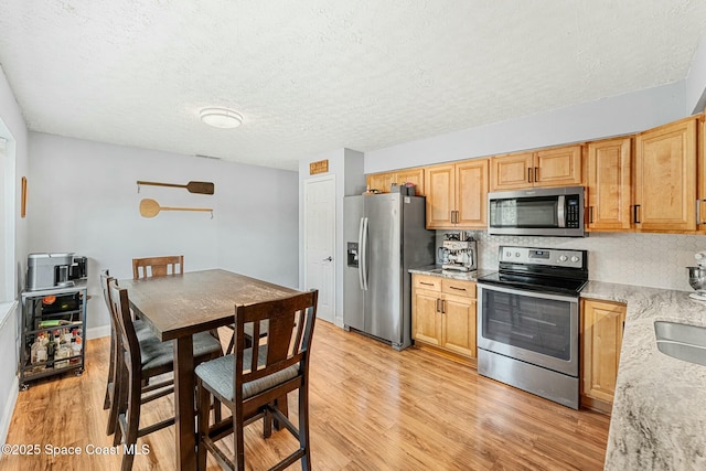 kitchen featuring light wood-style floors, light stone counters, stainless steel appliances, and a textured ceiling