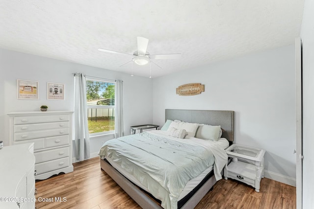 bedroom featuring light wood-type flooring, a ceiling fan, baseboards, and a textured ceiling