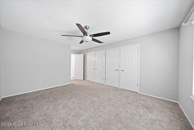 unfurnished bedroom featuring carpet, two closets, a ceiling fan, a textured ceiling, and baseboards