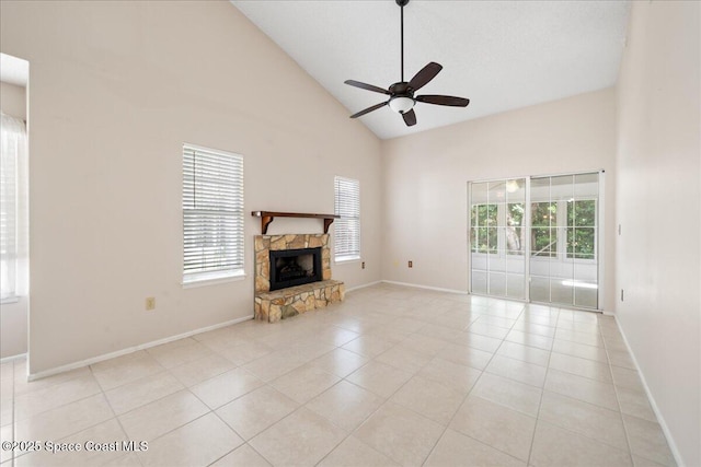 unfurnished living room with high vaulted ceiling, a stone fireplace, light tile patterned flooring, a ceiling fan, and baseboards