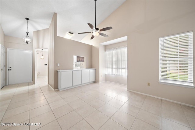 empty room featuring ceiling fan, high vaulted ceiling, baseboards, and light tile patterned flooring