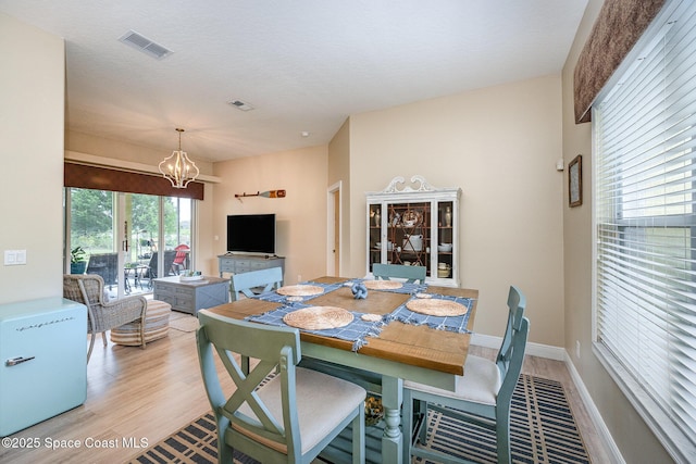 dining space with baseboards, light wood-style flooring, visible vents, and a notable chandelier