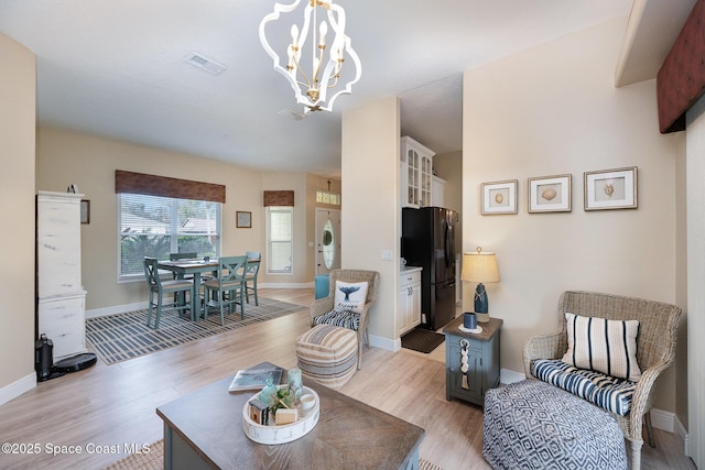 living area featuring light wood finished floors, stacked washing maching and dryer, visible vents, and an inviting chandelier