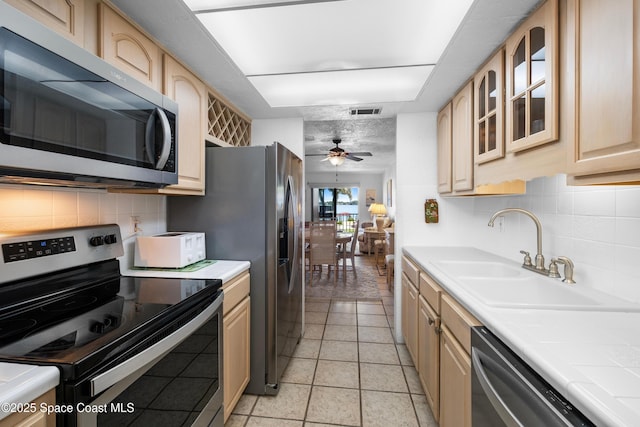 kitchen featuring visible vents, light brown cabinets, a sink, appliances with stainless steel finishes, and glass insert cabinets