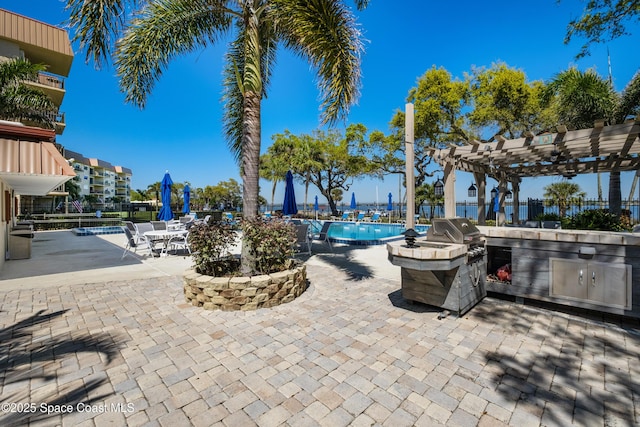 view of patio featuring fence, exterior kitchen, a community pool, area for grilling, and a pergola