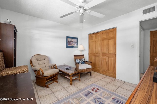 living area featuring light tile patterned floors, visible vents, a textured ceiling, and ceiling fan