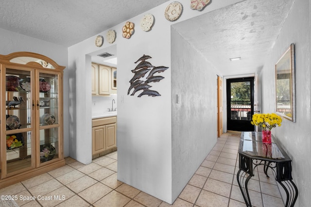 corridor featuring a sink, a textured ceiling, and light tile patterned floors