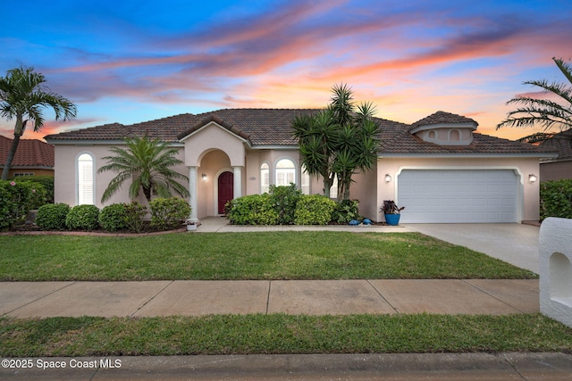 view of front of home with stucco siding, an attached garage, concrete driveway, and a yard