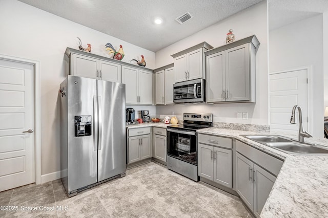 kitchen featuring a textured ceiling, gray cabinetry, stainless steel appliances, a sink, and visible vents