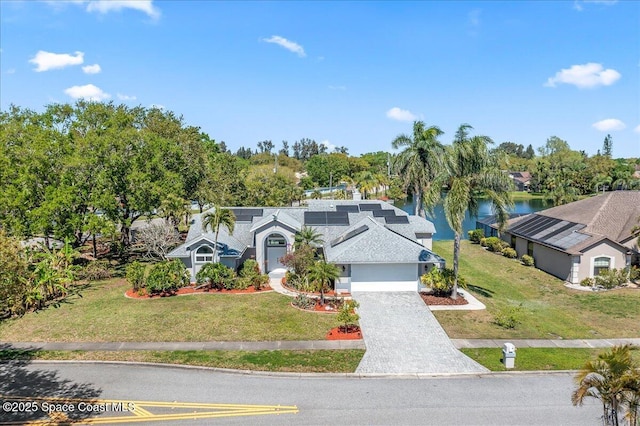 view of front of house with decorative driveway, a water view, solar panels, and a front yard