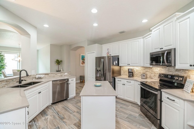 kitchen with tasteful backsplash, arched walkways, a kitchen island, appliances with stainless steel finishes, and a sink