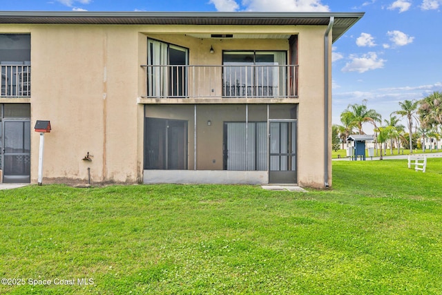 rear view of property with a balcony, stucco siding, and a yard