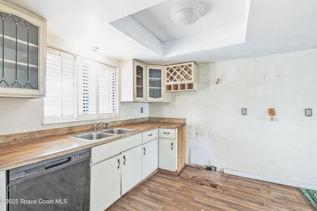 kitchen with wood finished floors, a sink, black dishwasher, a raised ceiling, and glass insert cabinets