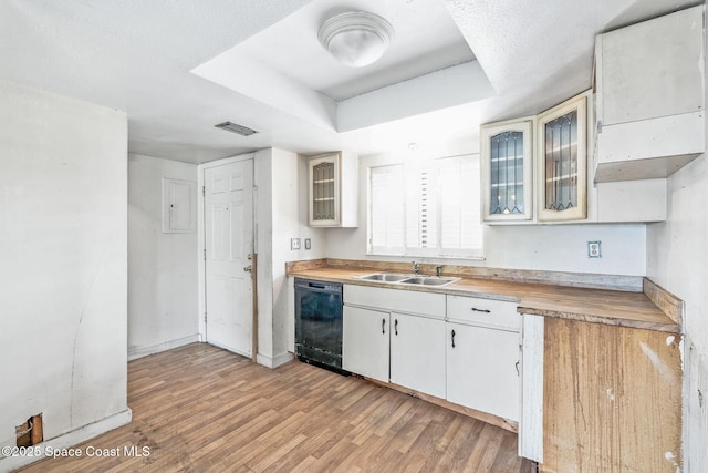 kitchen featuring a sink, visible vents, light wood-style floors, black dishwasher, and a tray ceiling