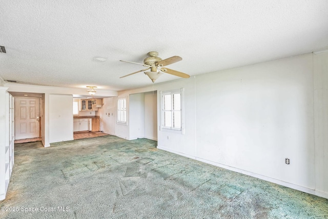 unfurnished living room with carpet floors, baseboards, a ceiling fan, and a textured ceiling