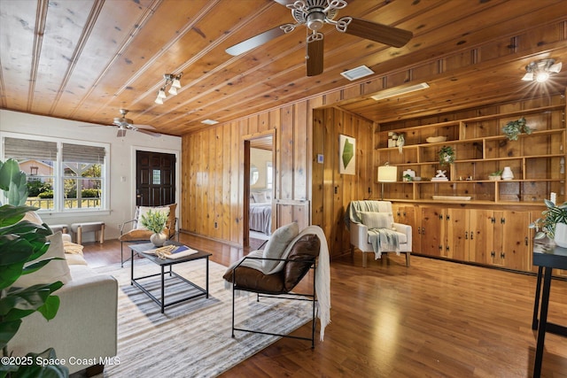 living area with ceiling fan, wood finished floors, wood ceiling, and wooden walls