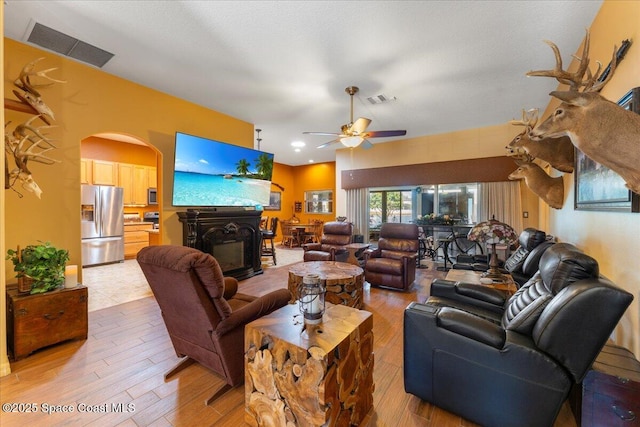 living room with arched walkways, light wood-style flooring, a fireplace, and visible vents