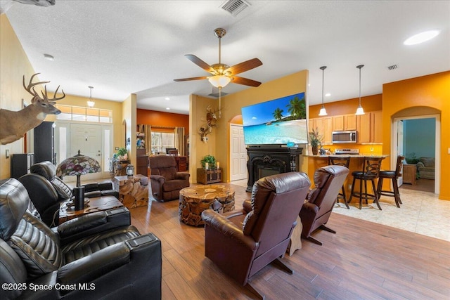 living room featuring light wood-type flooring, visible vents, a fireplace, and arched walkways