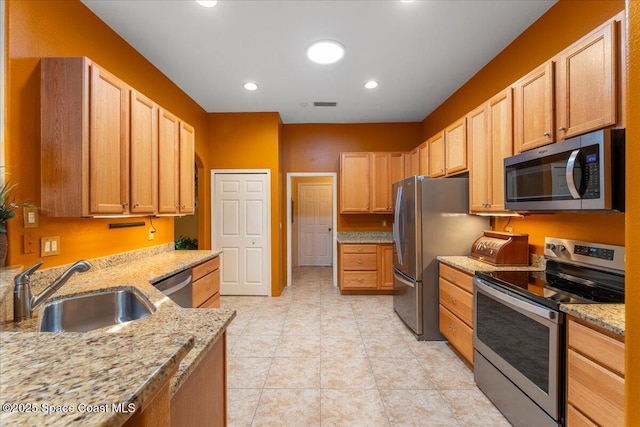 kitchen with light tile patterned floors, recessed lighting, a sink, appliances with stainless steel finishes, and light stone countertops