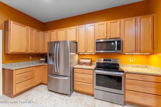 kitchen featuring light tile patterned floors, light stone counters, stainless steel appliances, and light brown cabinetry