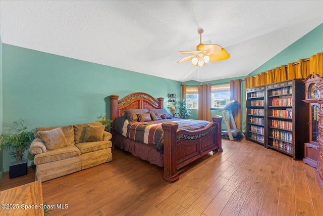 bedroom with lofted ceiling, hardwood / wood-style flooring, a textured ceiling, and a ceiling fan