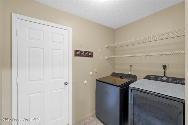 washroom with laundry area, baseboards, a textured ceiling, and washing machine and clothes dryer