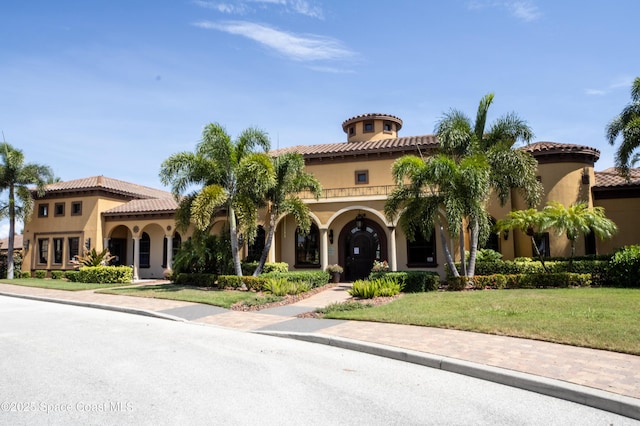 mediterranean / spanish house featuring a front yard, a tiled roof, and stucco siding