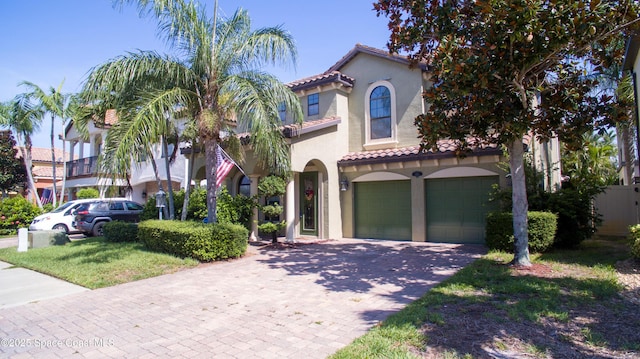 mediterranean / spanish-style house with an attached garage, a tiled roof, decorative driveway, and stucco siding