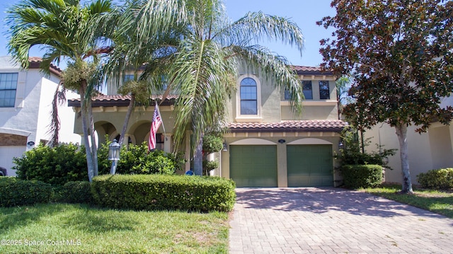 mediterranean / spanish house featuring an attached garage, a tile roof, decorative driveway, and stucco siding