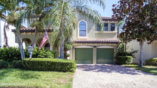 mediterranean / spanish house featuring a garage, a tiled roof, decorative driveway, and stucco siding