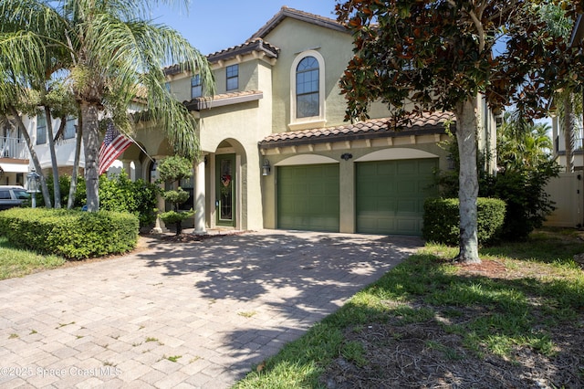 mediterranean / spanish home featuring driveway, an attached garage, a tile roof, and stucco siding