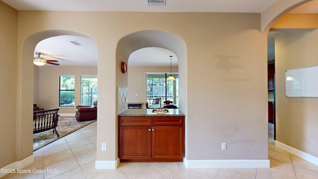 kitchen featuring light tile patterned floors, a ceiling fan, light stone countertops, and a healthy amount of sunlight