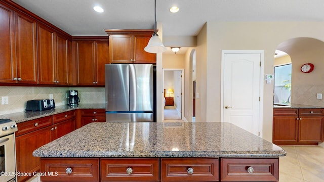 kitchen with light stone counters, a center island, arched walkways, light tile patterned floors, and freestanding refrigerator