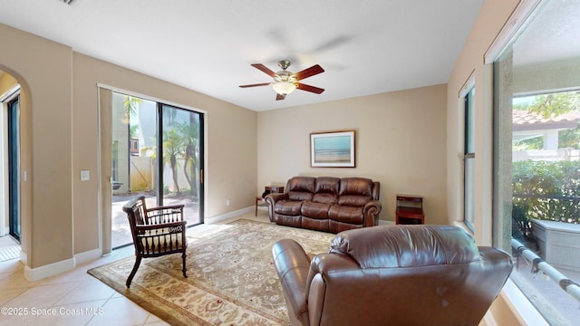 living area with baseboards, arched walkways, a ceiling fan, and light tile patterned flooring