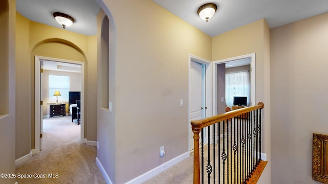 corridor with light carpet, baseboards, and arched walkways