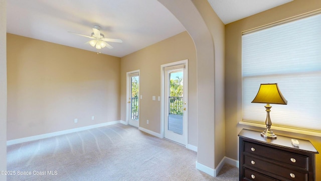 doorway to outside featuring arched walkways, light carpet, ceiling fan, and baseboards