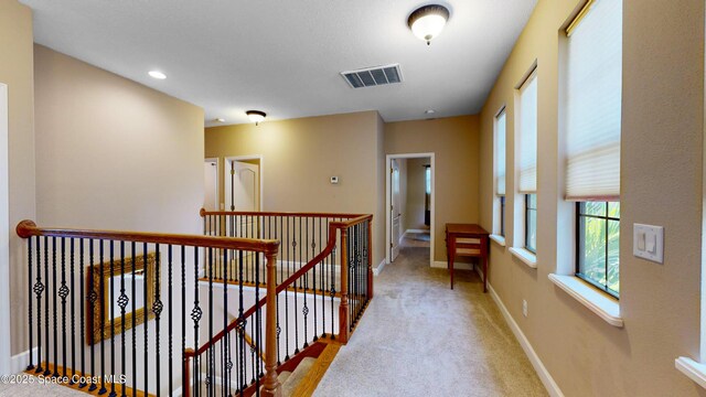 hall featuring carpet floors, baseboards, visible vents, and an upstairs landing