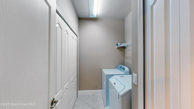 laundry room with washing machine and clothes dryer, light tile patterned floors, a textured ceiling, laundry area, and baseboards