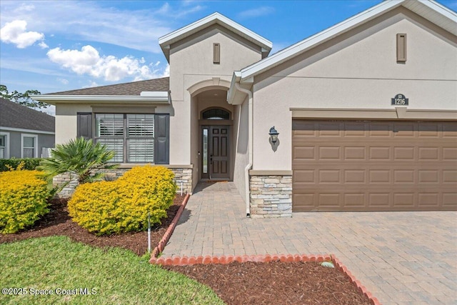 view of front of home featuring decorative driveway, stone siding, and stucco siding