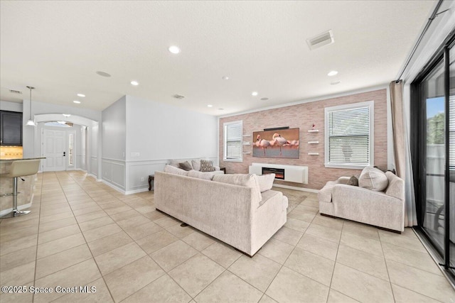 living area with arched walkways, a lit fireplace, light tile patterned floors, and visible vents