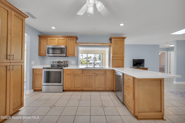 kitchen with a peninsula, stainless steel appliances, light countertops, and a sink